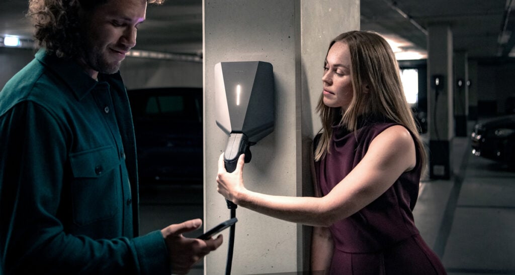 Man and woman handling Easee Charger in parking garage. 