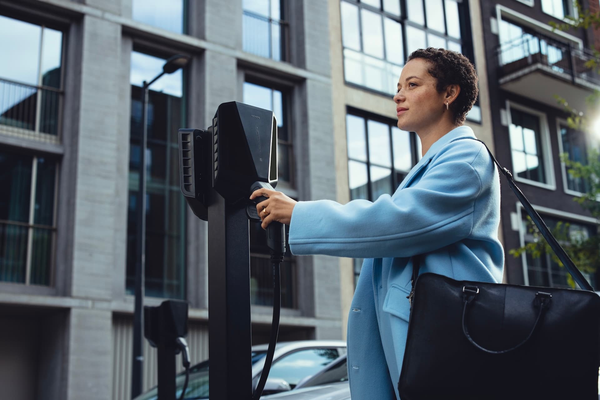 Vrouw plugt laadkabel in zwarte laadpaal voor elektrische auto's