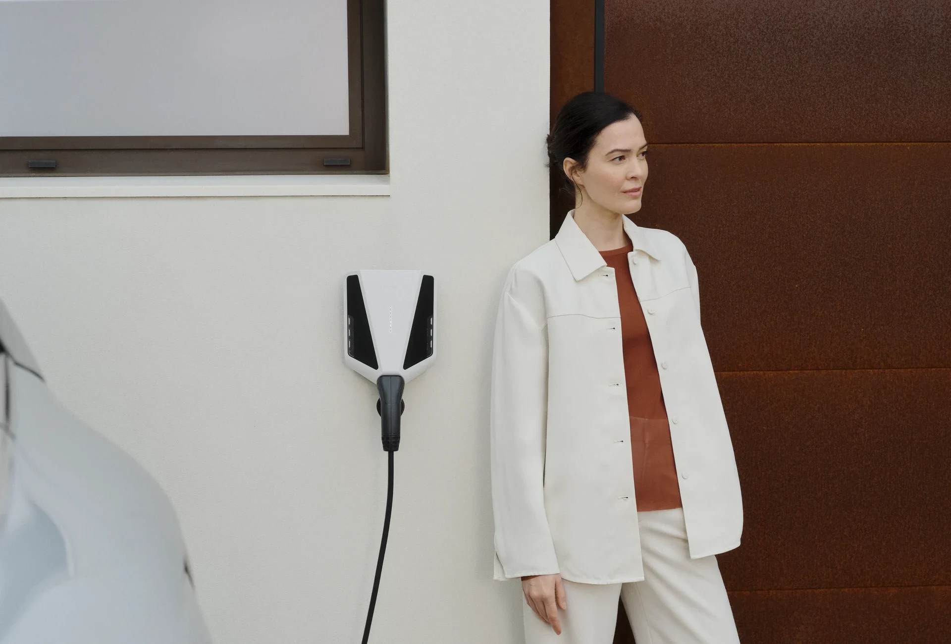 Vrouw staat naast een aan de muur gemonteerde Easee EV-lader die een elektrische auto oplaadt.
